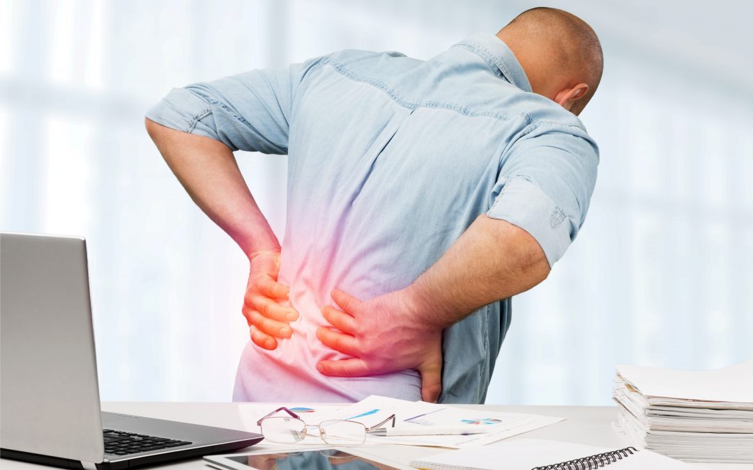Man at an office desk leaning forward and clutching his lower back, with a red highlight indicating pain.